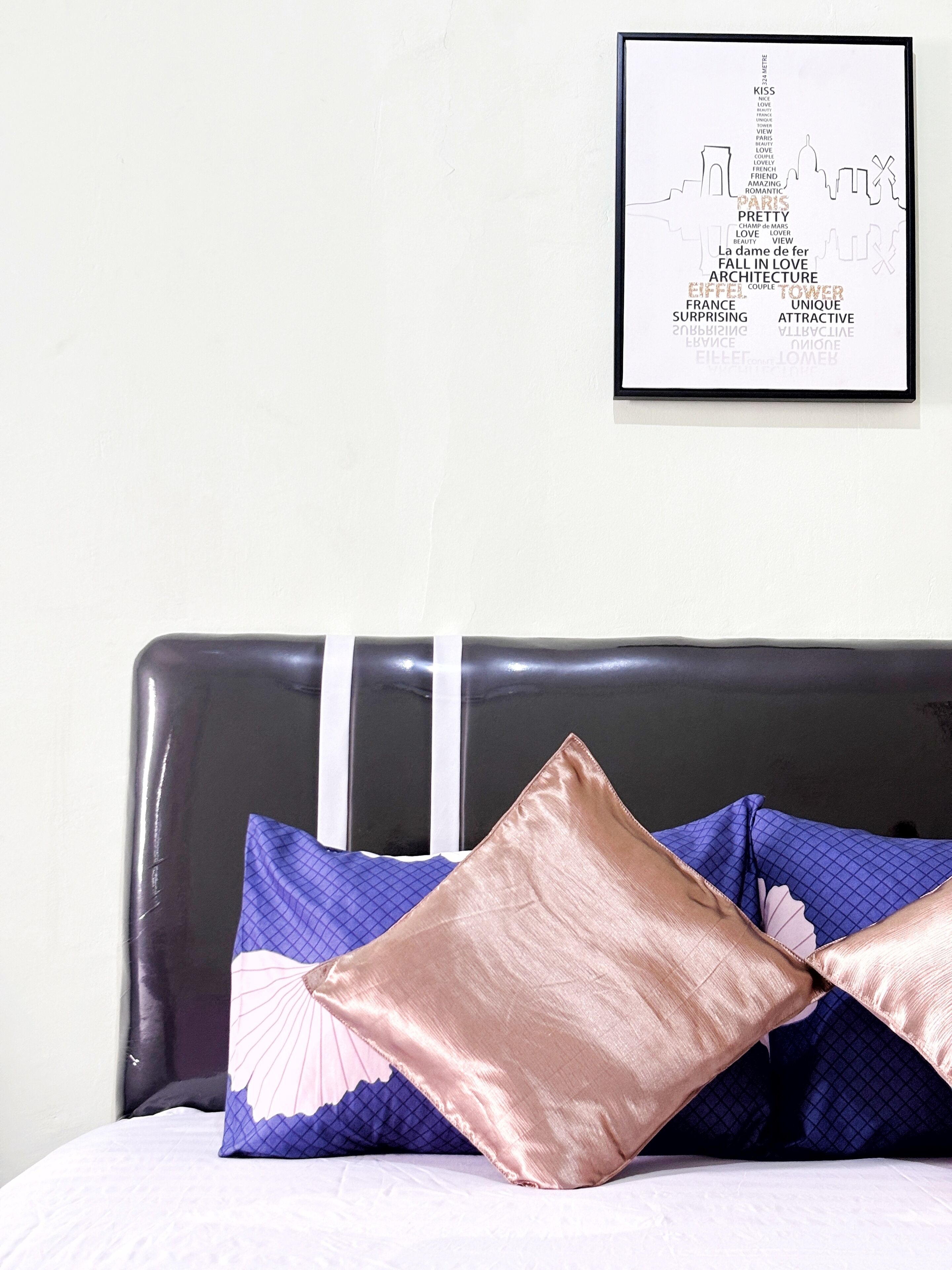A bed with a black headboard, two decorative pillows, and a framed word cloud on the wall.