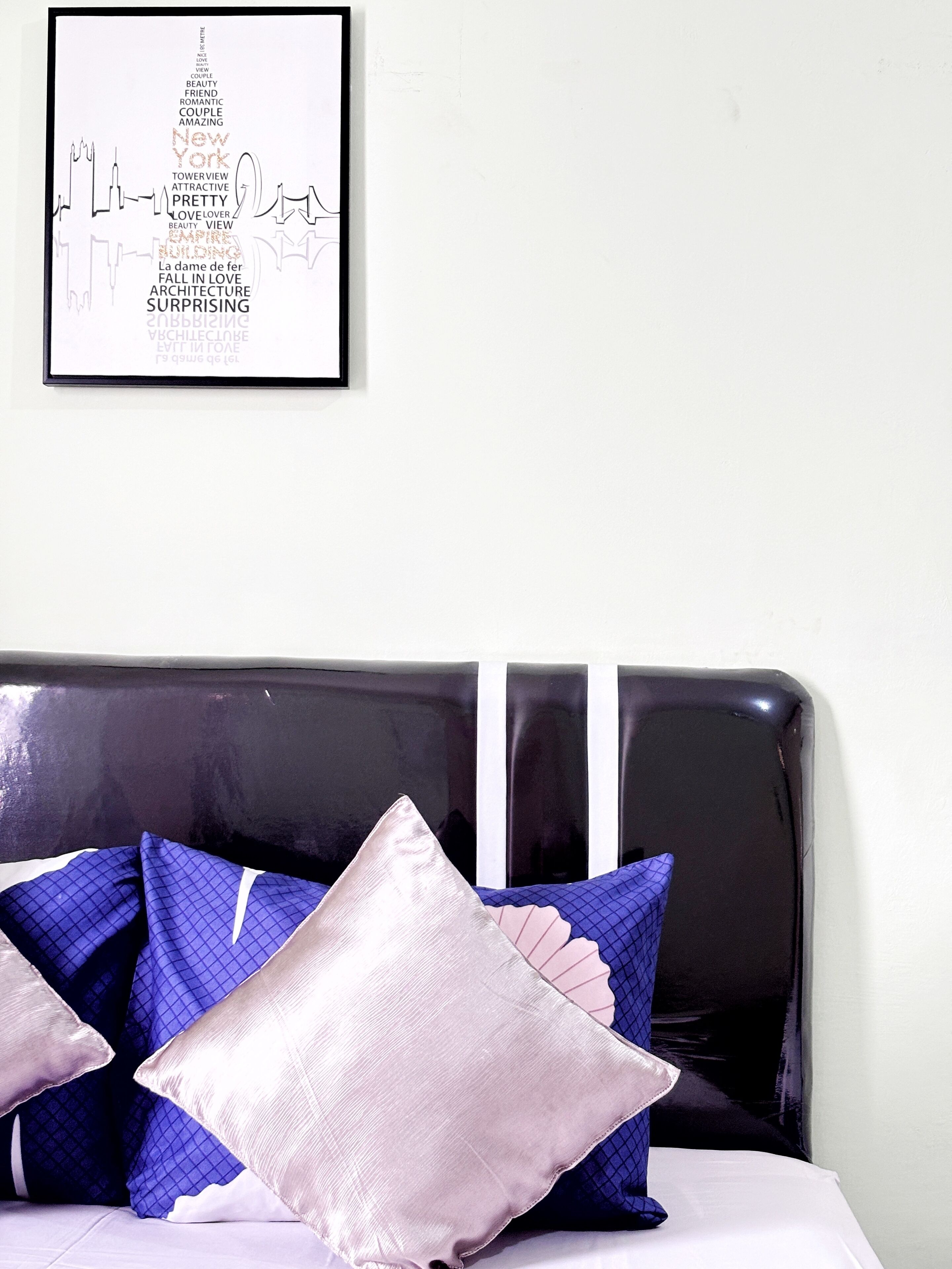 A neatly made bed with a black headboard and decorative pillows in shades of blue and pink.