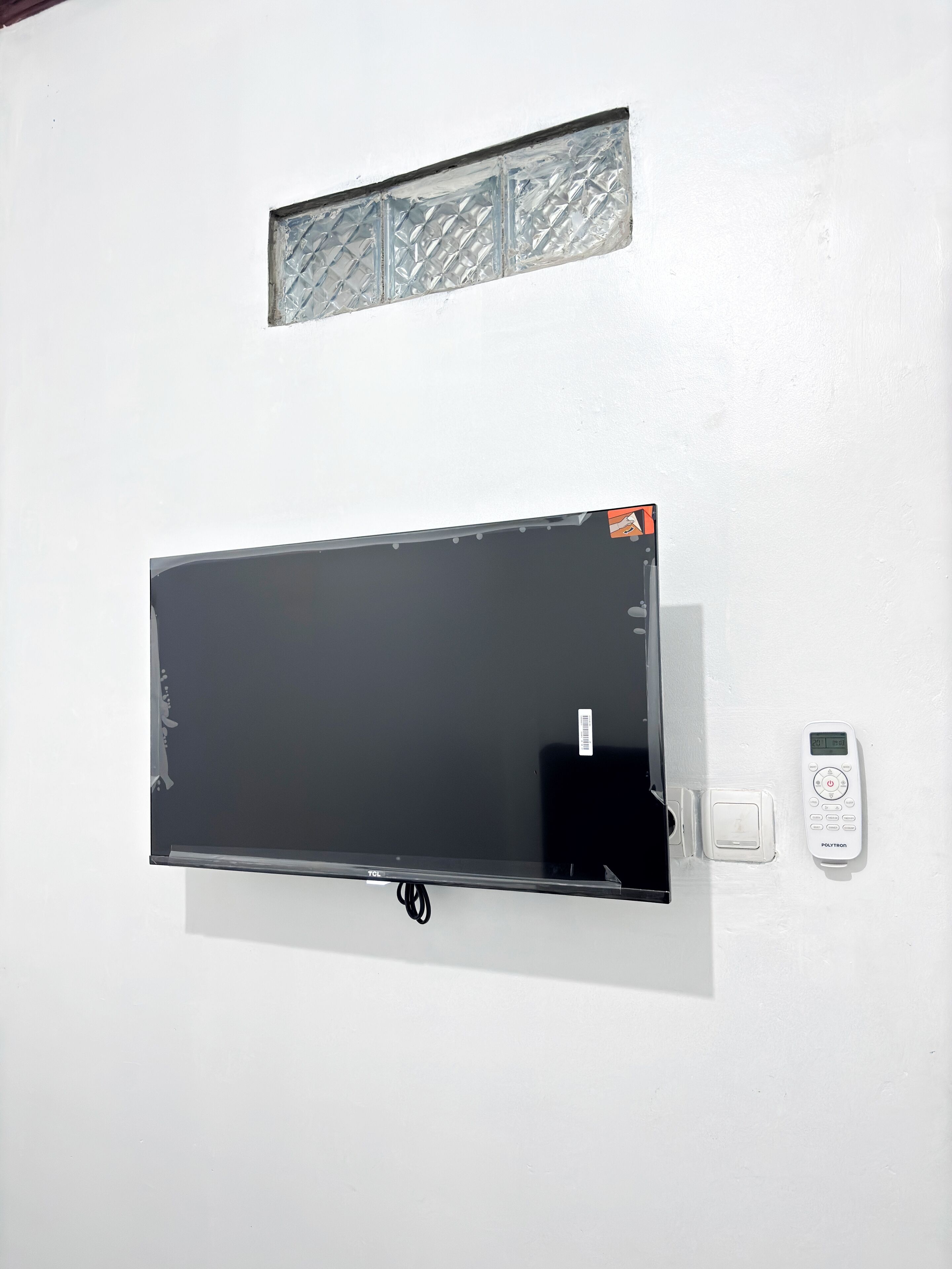 Una pared blanca con una pantalla negra grande, un control remoto blanco pequeño y un interruptor blanco pequeño.