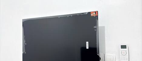 Una pared blanca con una pantalla negra grande, un control remoto blanco pequeño y un interruptor blanco pequeño.