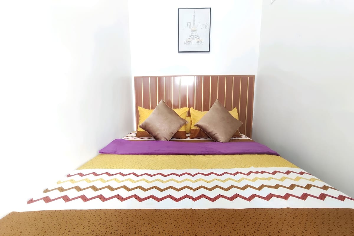 Cama bem arrumada com cabeceira listrada, colcha estampada e dois travesseiros.