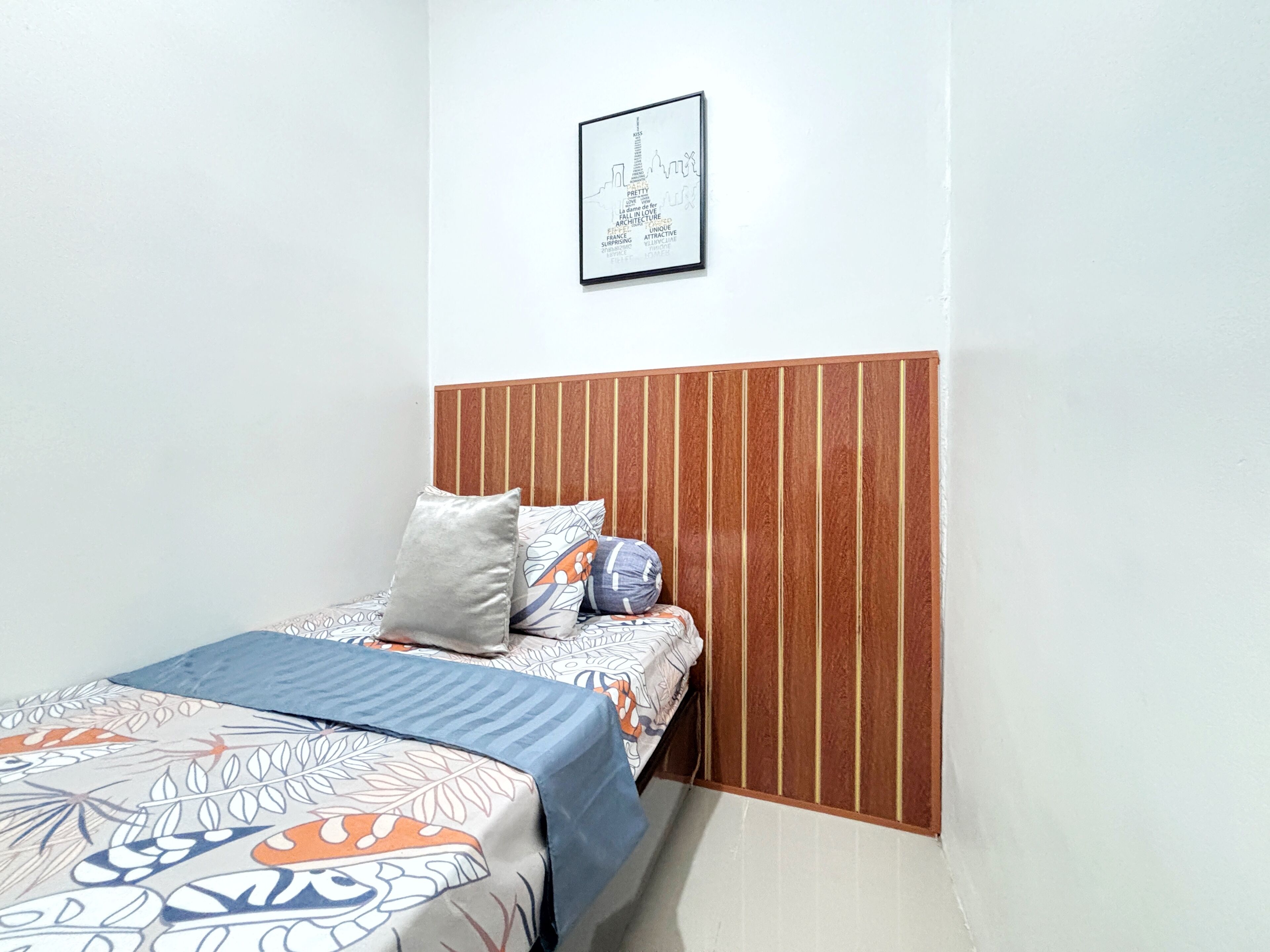 A bedroom with a bed, pillows, a wooden headboard, and a framed picture on the wall.