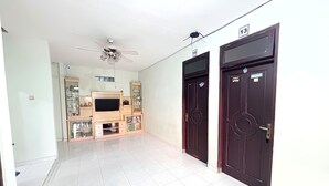 A hallway with a ceiling fan, a TV on a wooden entertainment unit, and two dark wooden doors. - Semarang Inn (Semarang)