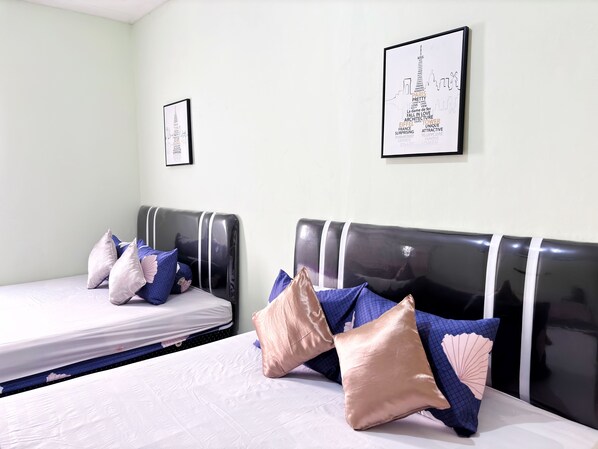 A hotel room with two beds, each with a headboard and multiple pillows. There are framed pictures on the walls. - Semarang Inn (Semarang)