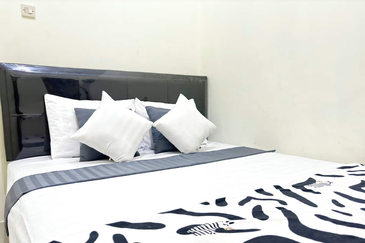Cama bem arrumada com colcha estampada em zebra, cabeceira cinza e travesseiros brancos e cinza escuro.