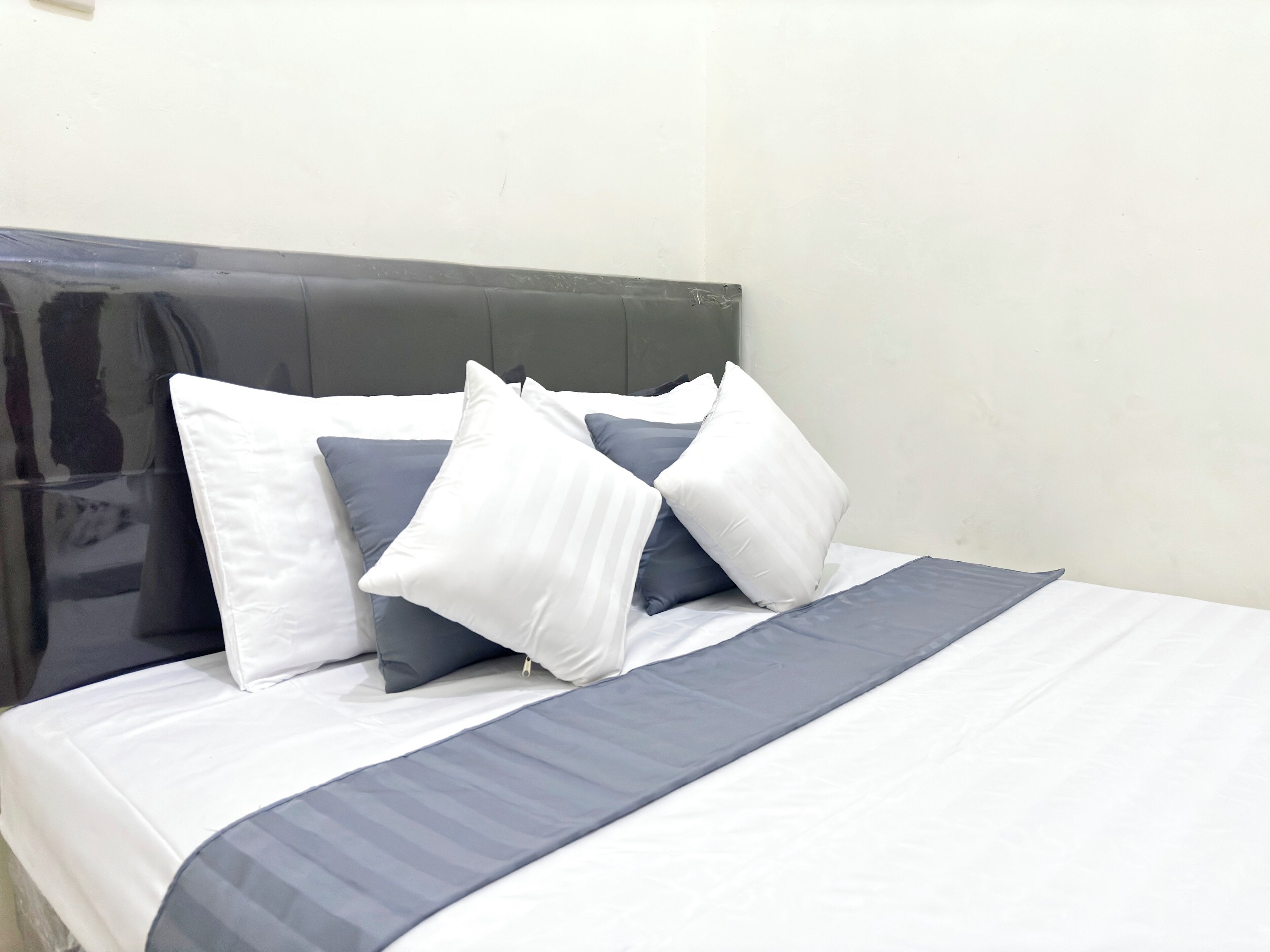 A neatly made bed with a grey and white striped bedspread and several pillows in shades of white and grey.