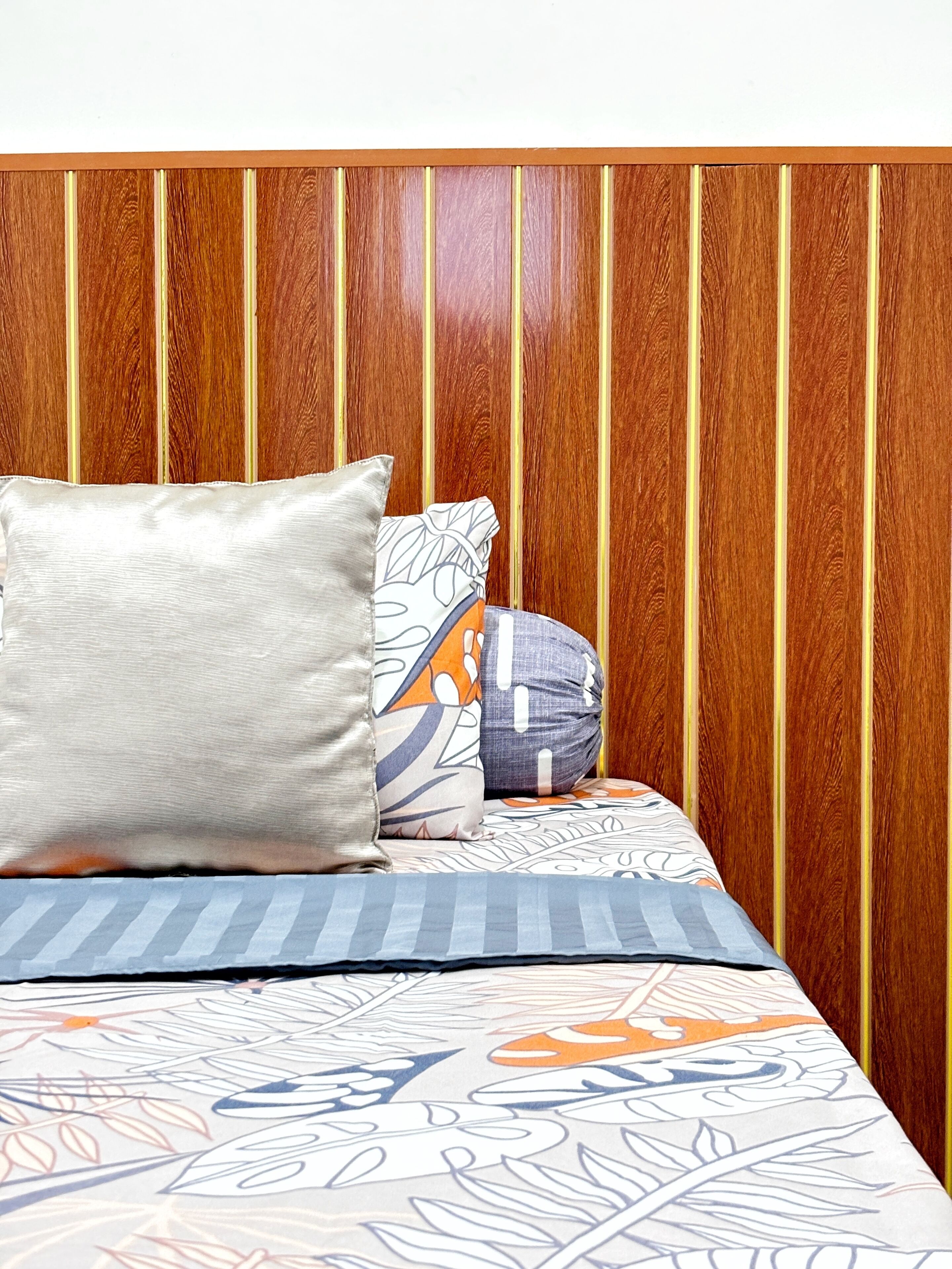 Una cama con colcha estampada y almohadas frente a un cabecero de madera.