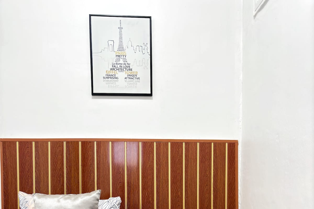Cama bem arrumada com roupa de cama estampada e almofadas, cabeceira de madeira e um quadro com vista para a cidade na parede.