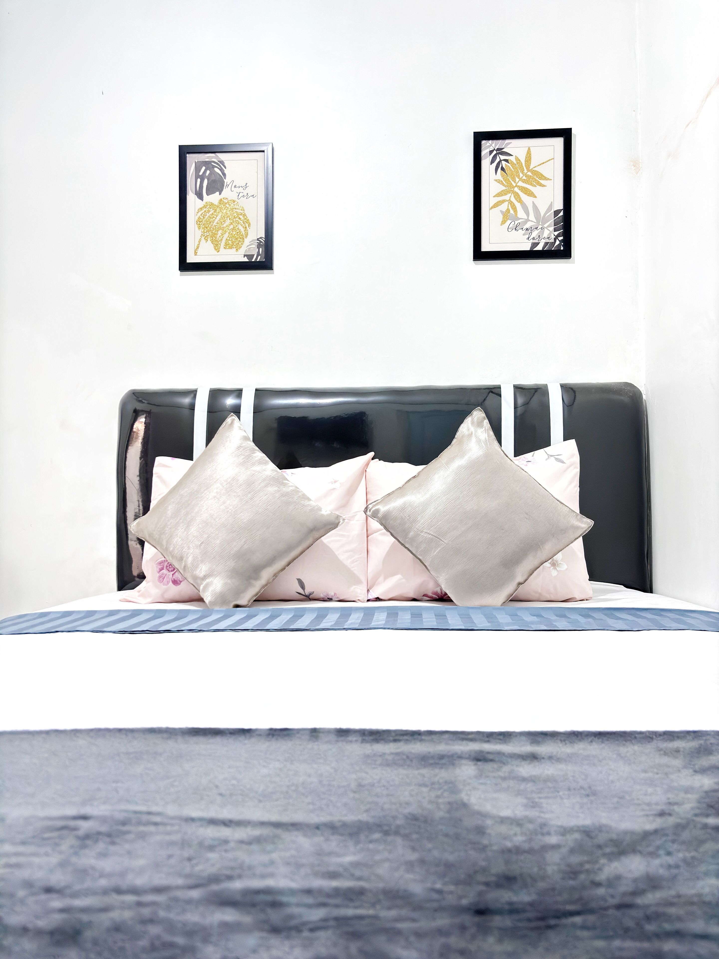 Un lit avec une tête de lit noire, deux œuvres d’art encadrées accrochées au mur et deux coussins.