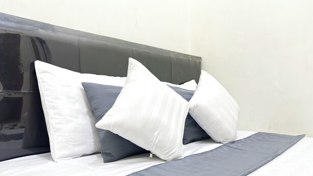 A neatly made bed with a grey and white striped bedspread and pillows in white and grey. - Semarang Inn (Semarang)