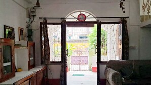 Een kamer met een houten kast, een bank en een deur die leidt naar een buitenruimte met een poort en groen.