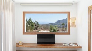 A flat-screen TV mounted on a wooden shelf with a view of a mountainous landscape through a window. - Villa Eos  (Castellammare del Golfo)