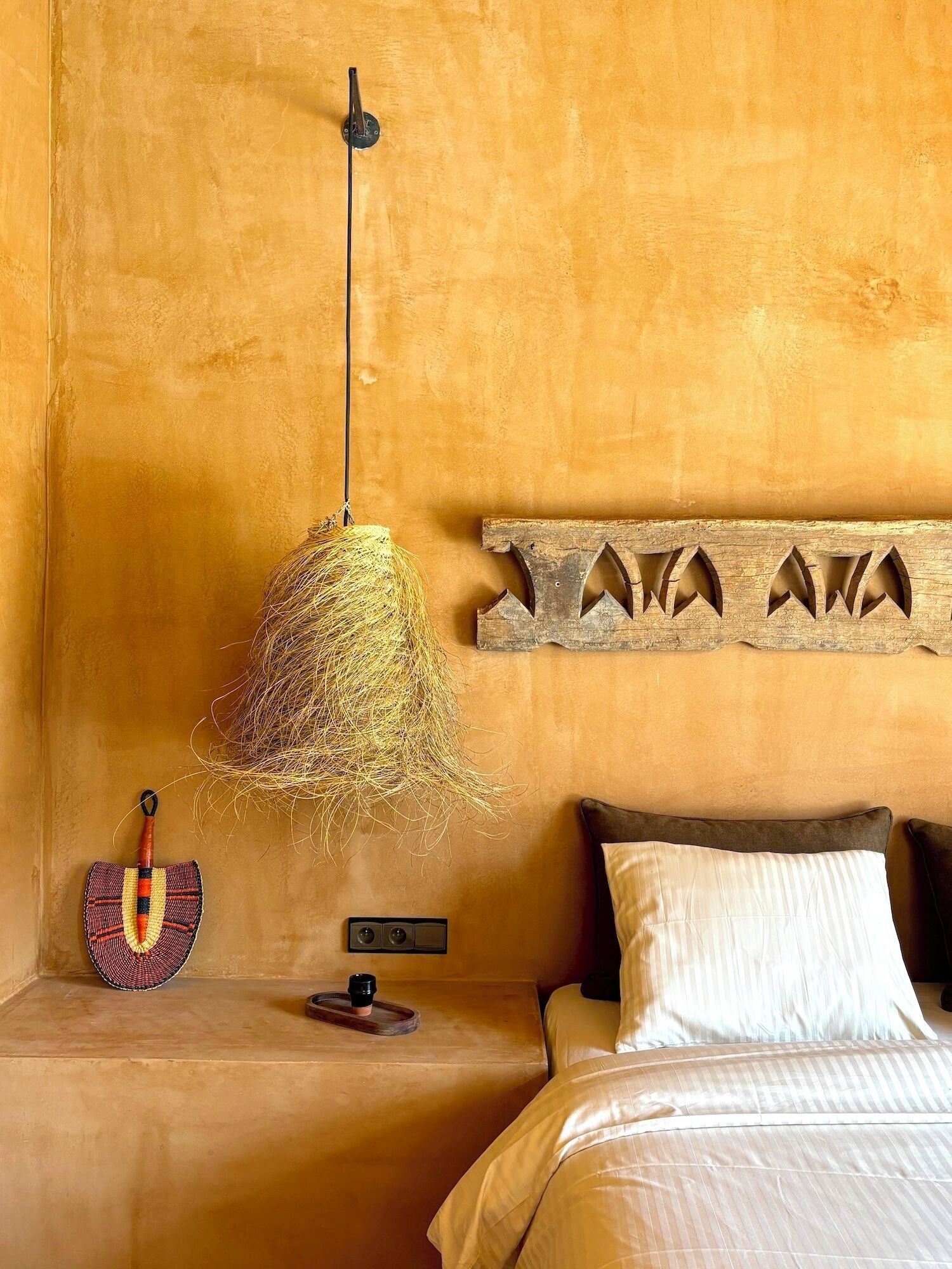 A room with a bed, a wooden headboard, a hanging light fixture, and a decorative wall piece.