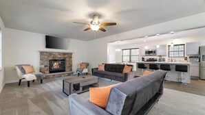 A modern living room with a fireplace, sofas, and a kitchen area with bar stools. - Pocono Mountain Escape! Fire pit•Hot tub•Games•Pool•Lake•Fishing•Golf•Ski•Hiking (Tobyhanna)