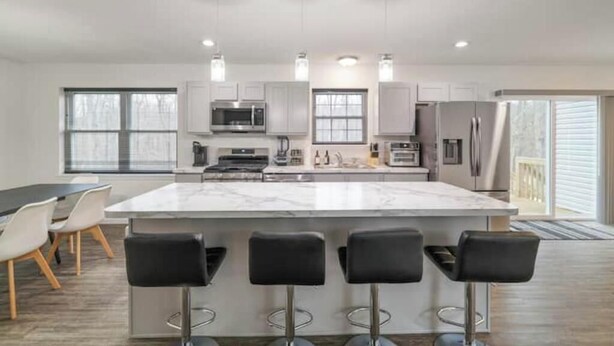 A modern kitchen with a large island, bar stools, stainless steel appliances, and pendant lighting. - Pocono Mountain Escape! Fire pit•Hot tub•Games•Pool•Lake•Fishing•Golf•Ski•Hiking (Tobyhanna)