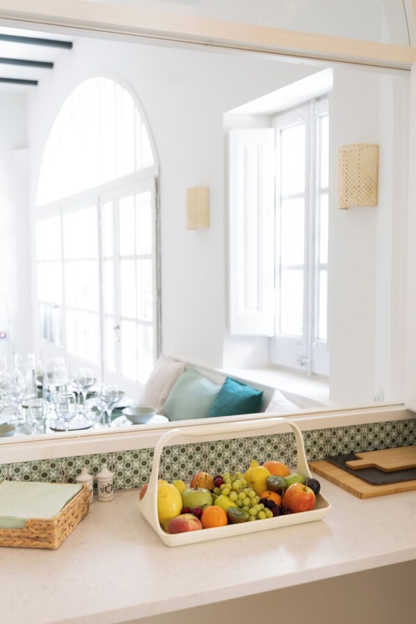 A kitchen with a fruit bowl, a cutting board, and a wicker basket on the counter.