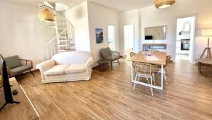 A spacious living area with a spiral staircase, a dining table with chairs, and a kitchen visible through an open door. - Villa Sapphires 94 (Plemmirio)