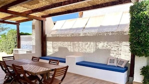 An outdoor patio with a wooden table and chairs, a built-in bench with cushions, and a view of the landscape. - Villa Sapphires 94 (Plemmirio)