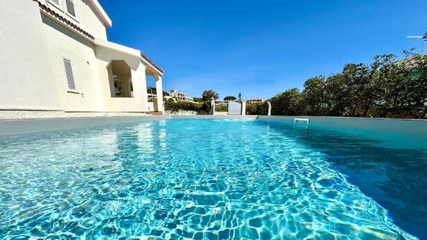 A clear swimming pool with a building on one side and trees on the other. - Villa Sapphires 94 (Plemmirio)