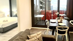 Quarto de hotel moderno com uma grande porta de vidro deslizante que dá para uma varanda com sofá vermelho e mesa de jantar.