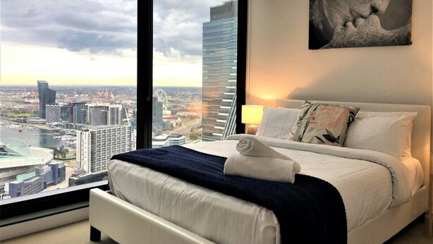 Quarto de hotel moderno com uma cama grande, vista para a cidade e um quadro na parede.