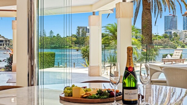A luxurious room with a view of a lake, a bottle of Moët & Chandon champagne, and a fruit platter on a glass table. - Main River Grandeur Mansion, 5 Bedroom, Pool & Sauna (Surfers Paradise)