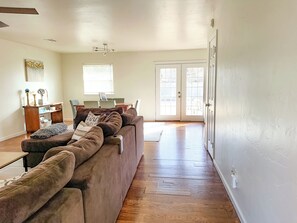A spacious living room with a large brown sectional sofa, a dining table with chairs, and a sliding glass door leading to an outdoor area.