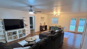 A living room with a large flat-screen TV, a dark-colored sofa, a small round coffee table, and a ceiling fan. - Walking distance to the Stadium! Charming 3-bedroom house in lovely Norman (Norman)