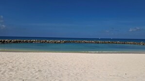 Una playa arenosa con un rompeolas rocoso y mar tranquilo.
