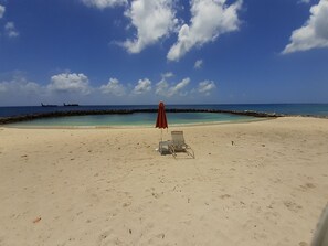 A beach with a clear sky, a red umbrella, and a chair. - 2 Bed Penthouse on Seven Mile Beach. Private Beach Cove, & 3 Pools! (#7) (Grand Cayman)