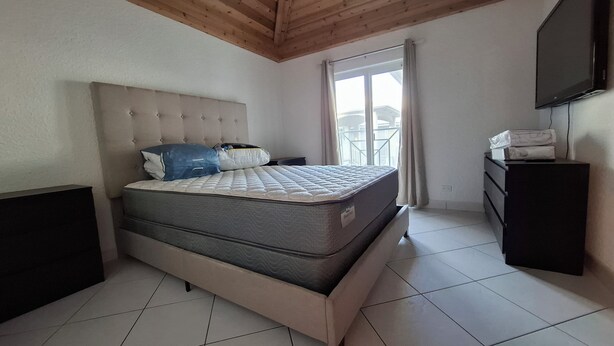 Un dormitorio con cama, cómoda, televisor y ventana con cortinas.