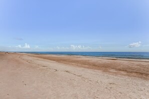Une vaste plage de sable fin, sous un ciel bleu dégagé et une mer calme.