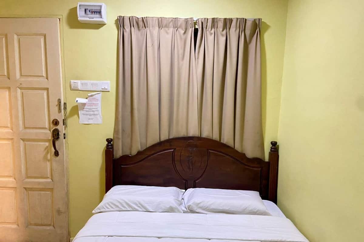 A room with a wooden bed, beige curtains, a wall-mounted thermostat, and a door with a handle.