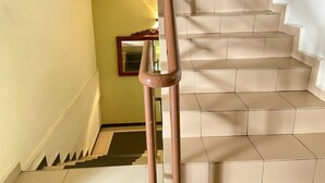 Una escalera con baldosas color beige y barandal marrón, que lleva a un rellano con un espejo y una mesita.