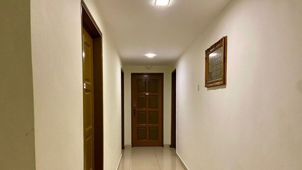 Un pasillo con piso de baldosas, una puerta de madera al final y un cuadro en la pared.