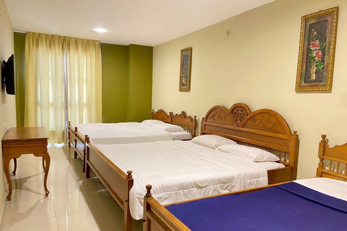 A hotel room with two wooden beds, a small table, and a television on the wall.
