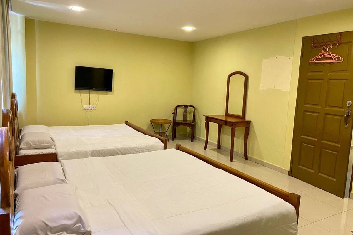 A hotel room with two single beds, a television, a wooden chair, a mirror, and a door with a hanger.