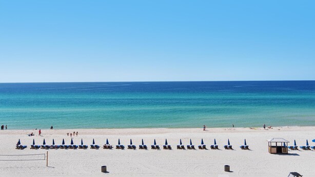 Een strand met rijen ligbedden en parasols, een redershut en een helder uitzicht op de oceaan.