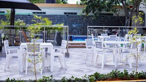 An outdoor patio area with white plastic chairs and tables, a swimming pool, and a view of a building with a stone facade. - Villas Vallejuelo (Vallejuelo)
