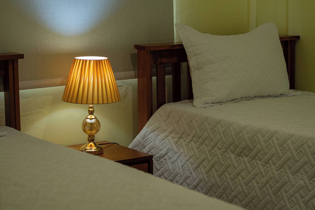 A hotel room with two beds, a bedside lamp, and a wooden nightstand.