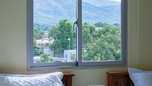 A room with a bed, a nightstand, and a window with a view of green hills and buildings. - Villas Vallejuelo (Vallejuelo)