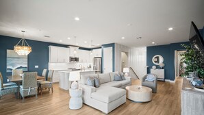 Ein modernes Wohnzimmer mit Ecksofa, Essbereich und einer Küche im Hintergrund.