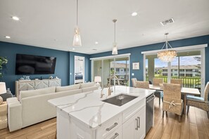 A modern kitchen with a marble island, white cabinetry, and a dining area with wicker chairs. - Seychelles ala SkyRun elegance (Naples)