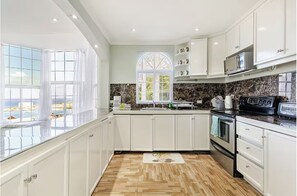 Une cuisine moderne avec des meubles blancs, une grande fenêtre et une vue sur la plage.