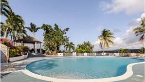 A swimming pool with a gazebo, palm trees, and a stone wall. - Cozy 1-bedroom apartment in Ocho Rios stunning views of the Caribbean sea. (Ocho Rios)