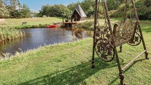 A rustic wooden structure by a pond, a swing with ornate metalwork, and a red boat. - 4 Star Holiday Home in Jerup (Jerup)