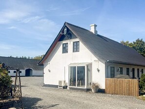 A single-story building with a sloped roof, a large glass door entrance, and a wooden fence. - 4 Star Holiday Home in Jerup (Jerup)