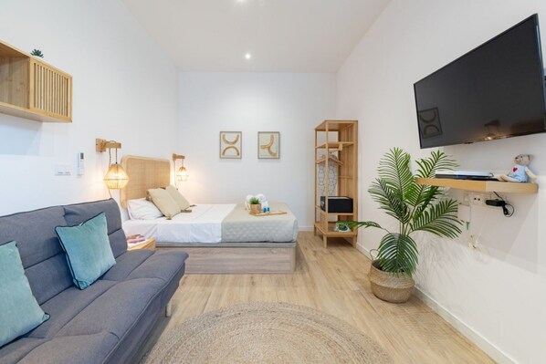 A modern, well-lit bedroom with a sofa, a bed, a TV, and a shelf with a plant.