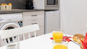 A kitchen with a washing machine, microwave, and a table with a glass of orange juice and a pastry. - Travel Habitat Ruzafa Loft 5 WIFI+AACC (Valencia / València)