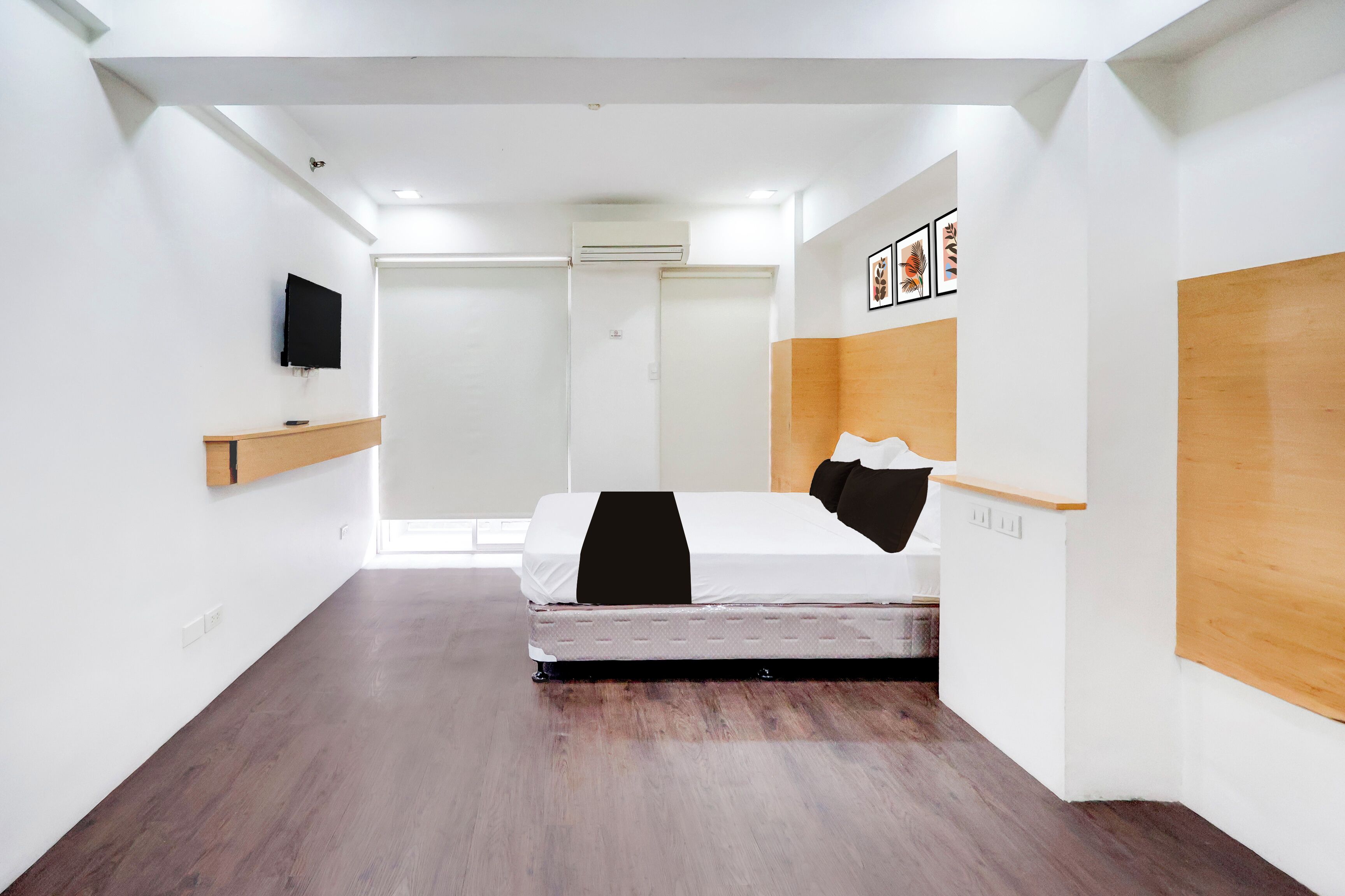 A modern hotel room with a bed, a mounted TV, and artwork on the walls.